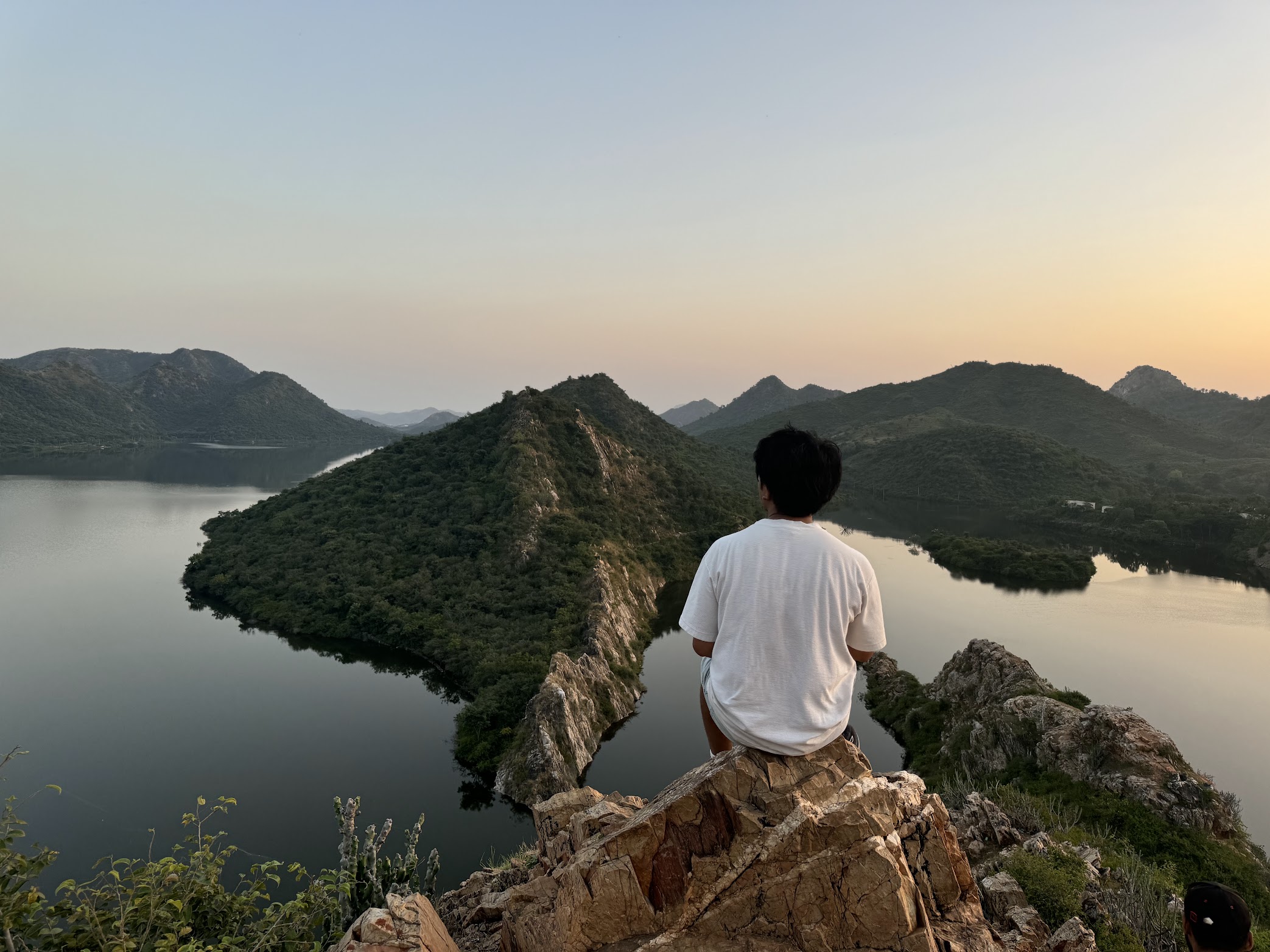 A boy sitting on a hill top looking over a sunset by the lake in India